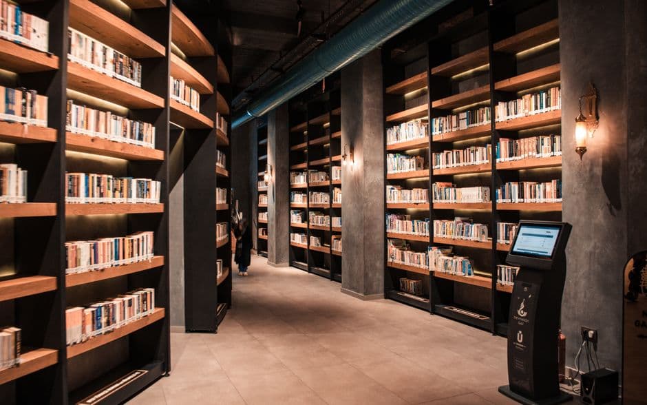 A spacious library featuring tall wooden bookshelves filled with books and ambient lighting.