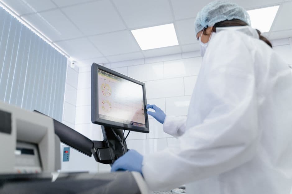 Woman in lab coat using touchscreen monitor in a modern laboratory setting.