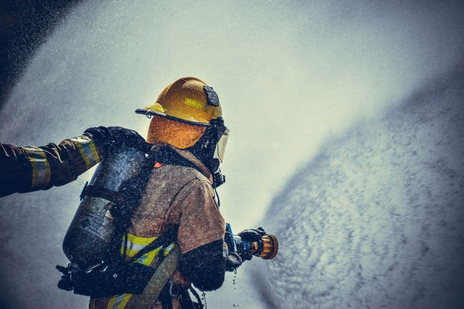 A brave firefighter in protective gear sprays water during training or emergency.