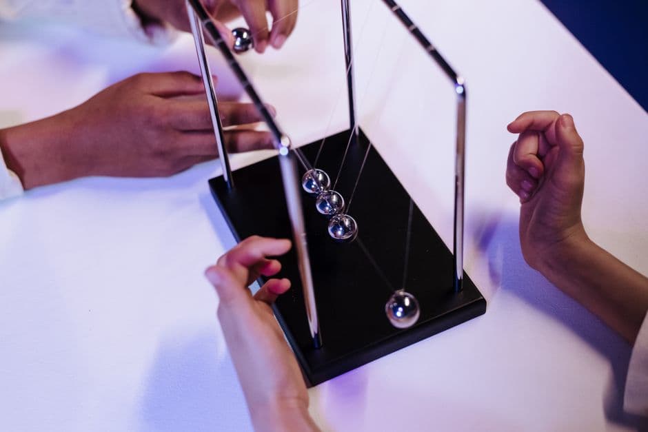 Close-up of hands interacting with a Newton's cradle on a white table in a studio setting.
