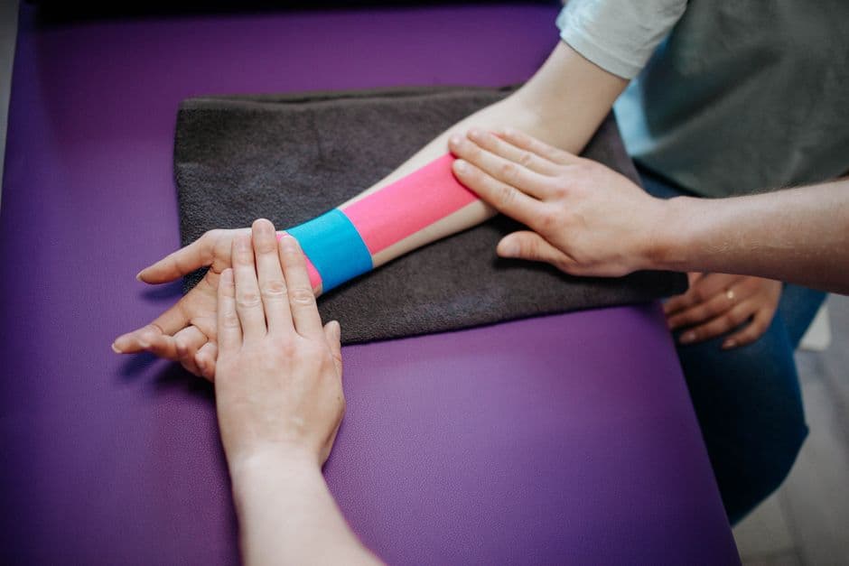 A therapist carefully applying colorful kinesiology tape on a patient's forearm for supportive therapy.