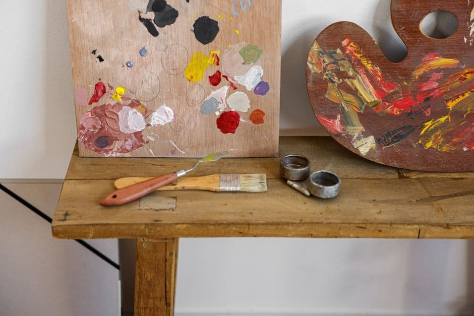 An artist's palette and brushes on a rustic wooden table, showcasing vibrant paint colors.