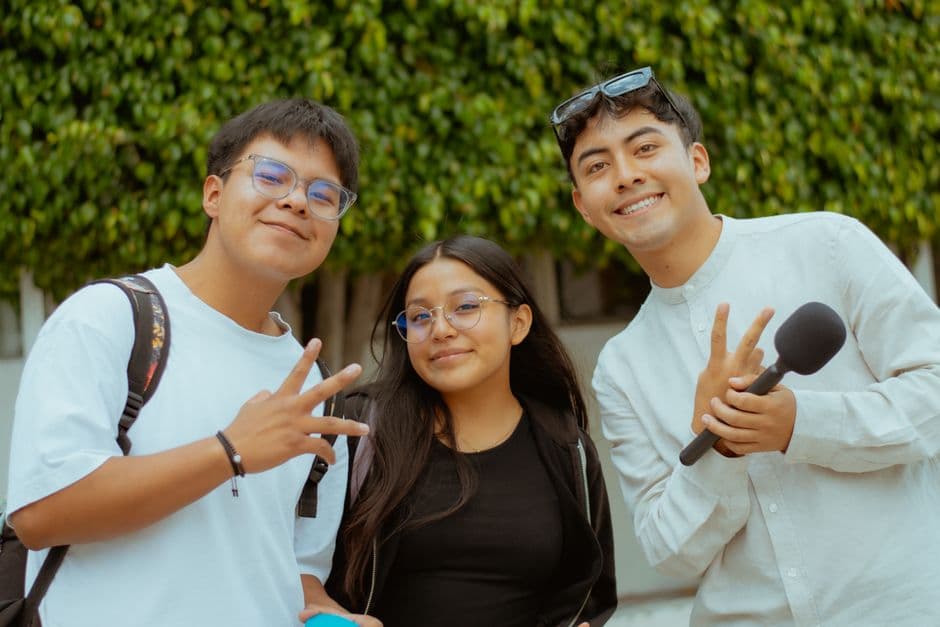 Three young adults smiling and posing outdoors, holding a microphone, showcasing a joyful moment.