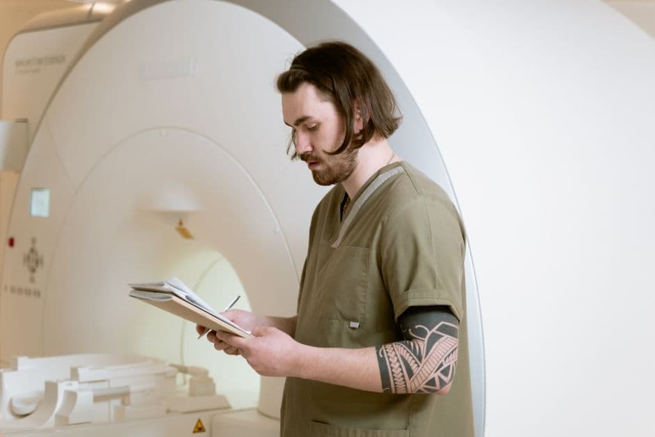 Radiology technician taking notes beside an MRI machine in a modern medical facility.