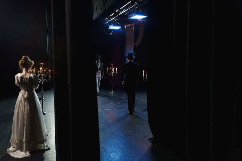 A captivating backstage view of actors in vintage costumes performing on a dimly lit theater stage.
