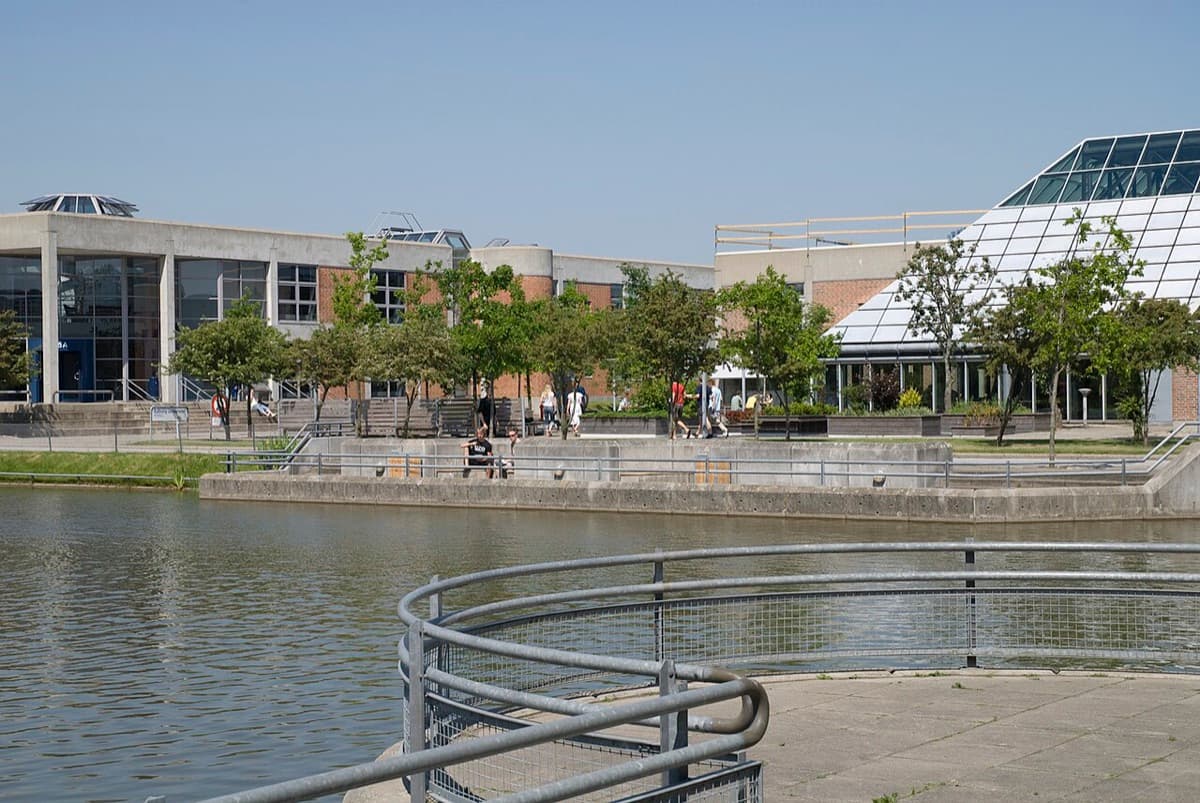Aalborg University campus by the water in summer with modern buildings reflected in lake.