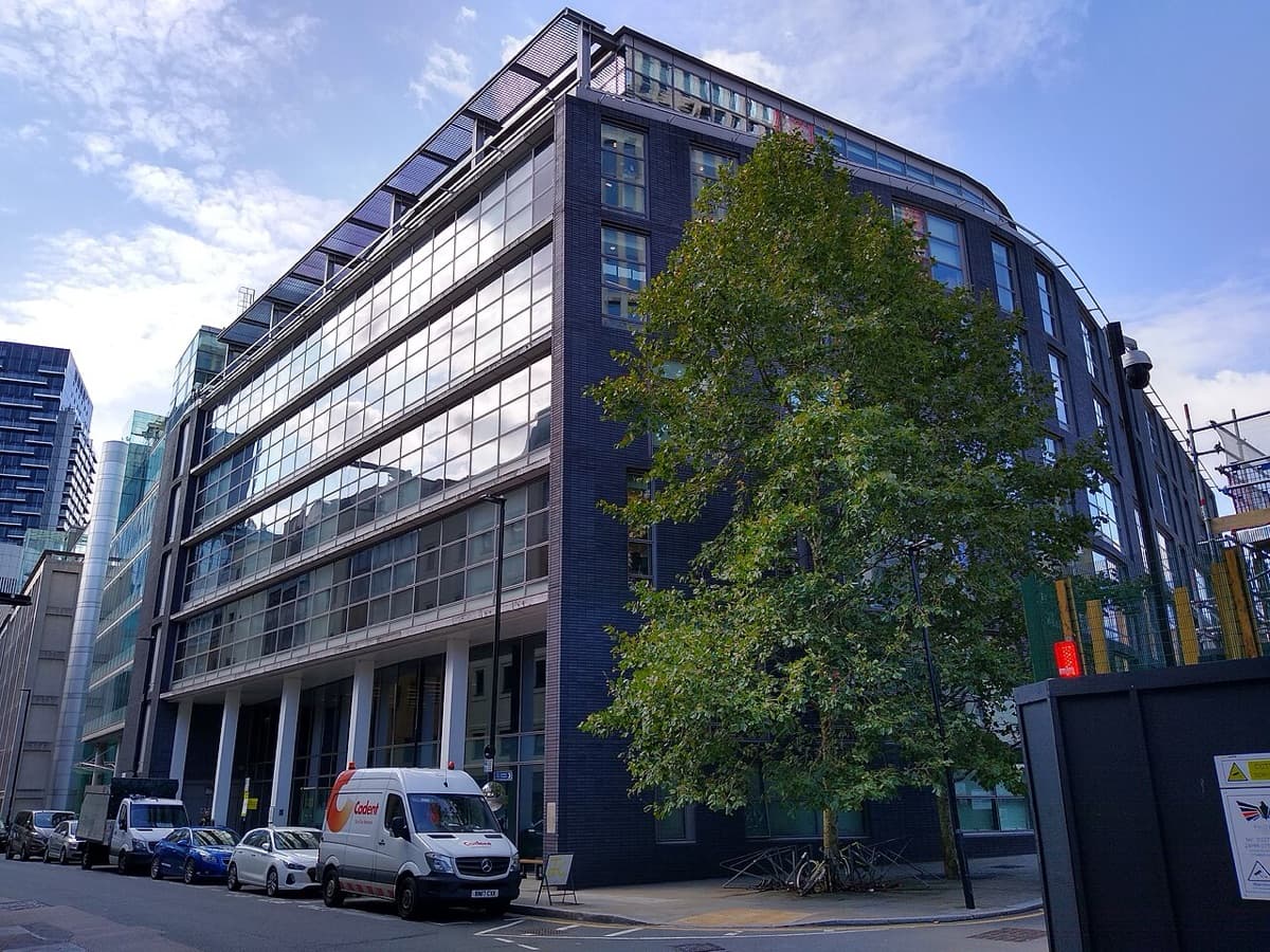 Modern Cass Business School building exterior in London with glass and brick facade, framed by mature trees.