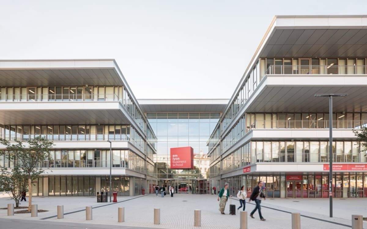 emlyon business school modern campus plaza showing contemporary architecture with 'emlyon' signage visible, featuring glass and metal design in daylight.