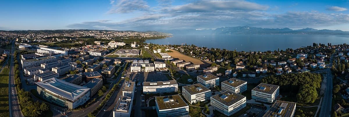 Aerial view of EPFL campus in Lausanne with modern buildings, Lake Geneva, and Alpine mountains.