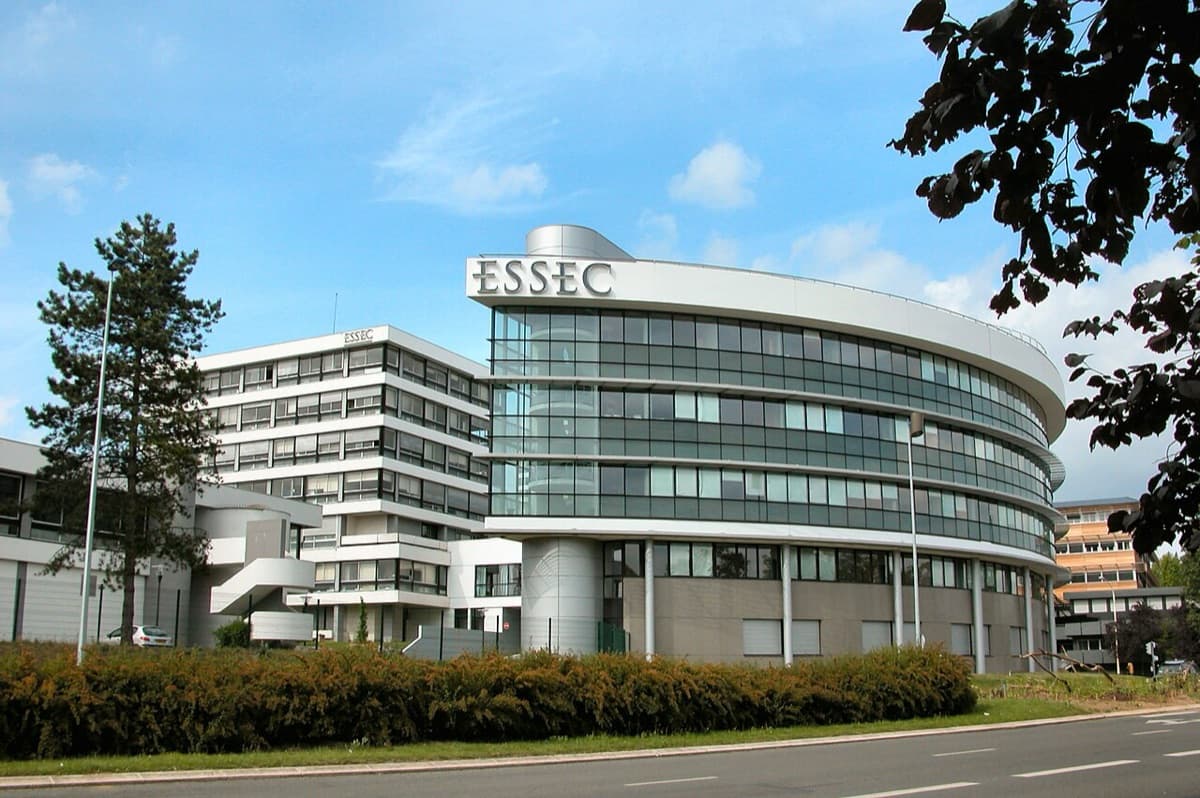 ESSEC Business School campus showing the distinctive curved modern building facade with grid pattern windows and landscaping in daylight.