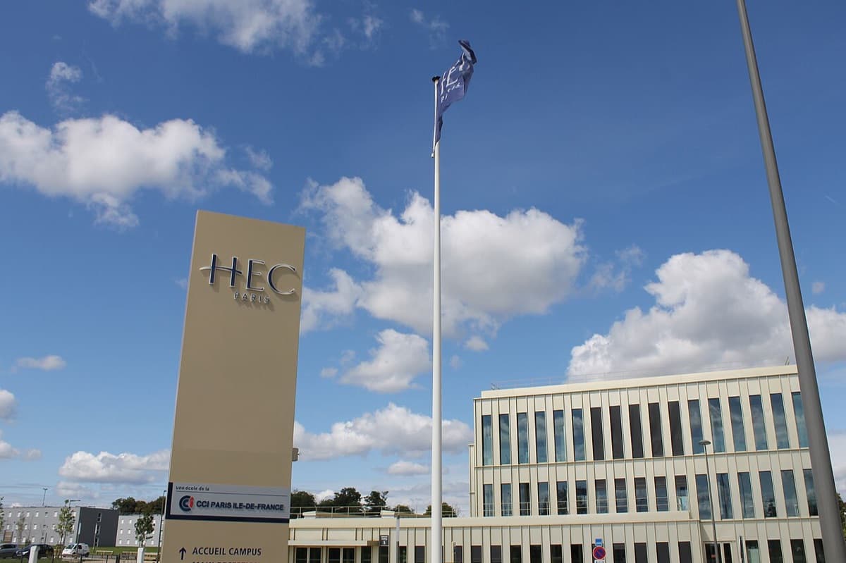 HEC Paris campus entrance featuring large sign with 'HEC PARIS' branding and modern building architecture in clear daylight.