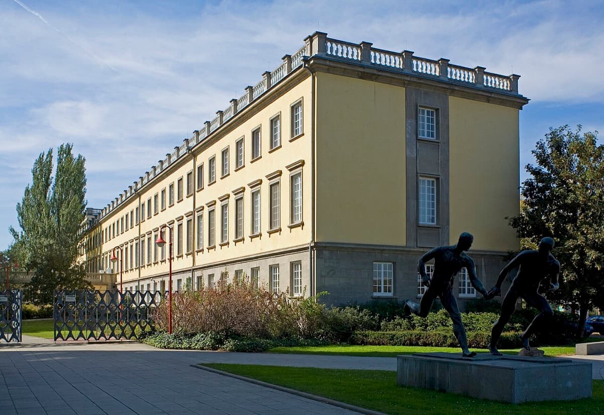 Yellow neoclassical University House building of HHL Leipzig with surrounding architecture and courtyard.