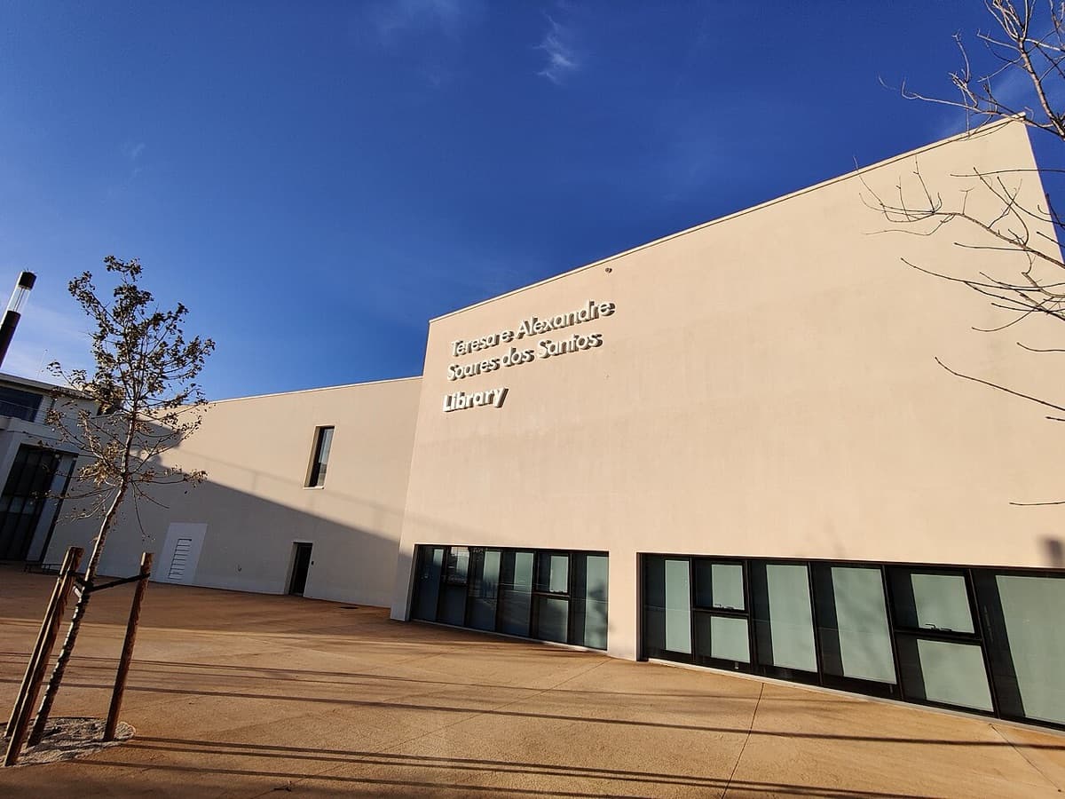 Modern library building at NOVA School of Business and Economics in Carcavelos, Portugal, with cream-colored facade and horizontal composition beneath blue sky.