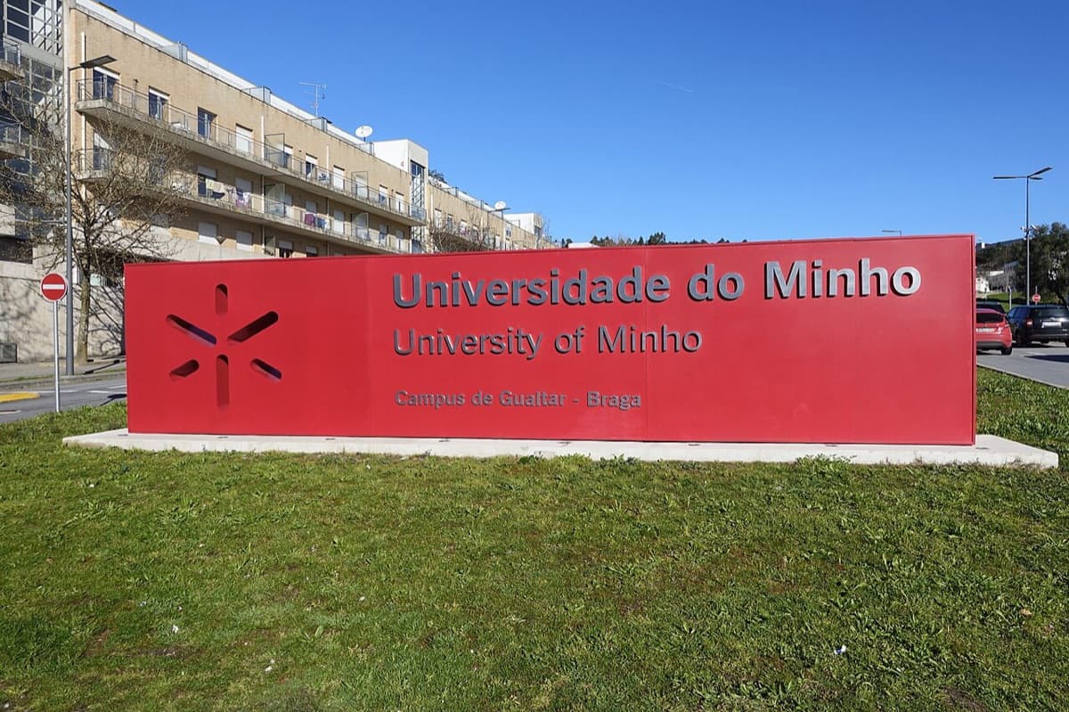 University of Minho Gualtar campus sign in red with institutional buildings visible in background on campus grounds in Braga, Portugal.