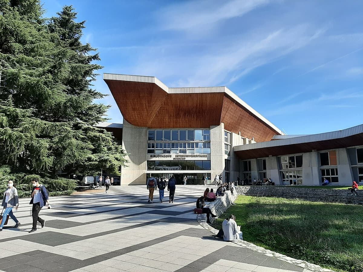 Modern glass-roofed library building with distinctive copper/red architectural elements on the Université Grenoble Alpes campus.