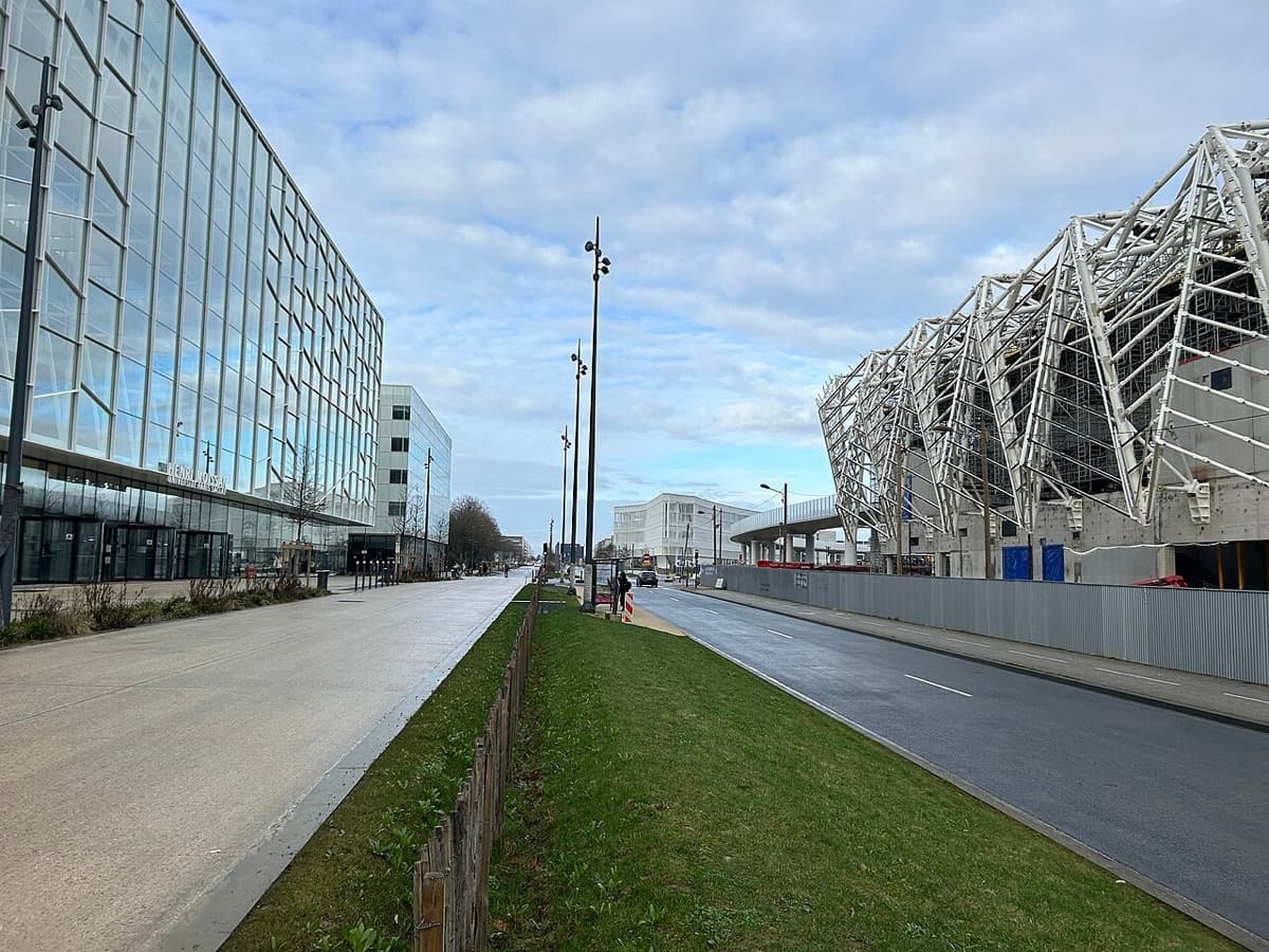 Wide pedestrian avenue lined with modern campus buildings at Université Paris-Saclay, with green space and contemporary architecture.