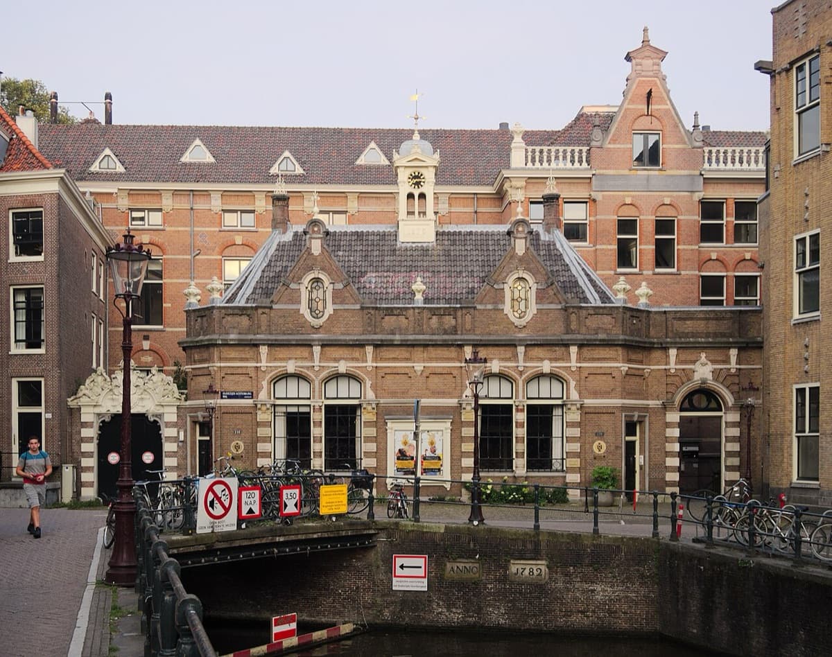 Distinctive facade of University of Amsterdam building with clock tower along Amsterdam canal, showing brick and classical architecture.