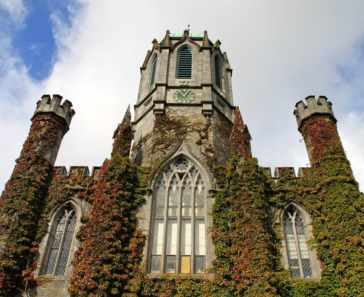 Historic tower building with ivy-covered stonework and clock face at University of Galway in autumn light.