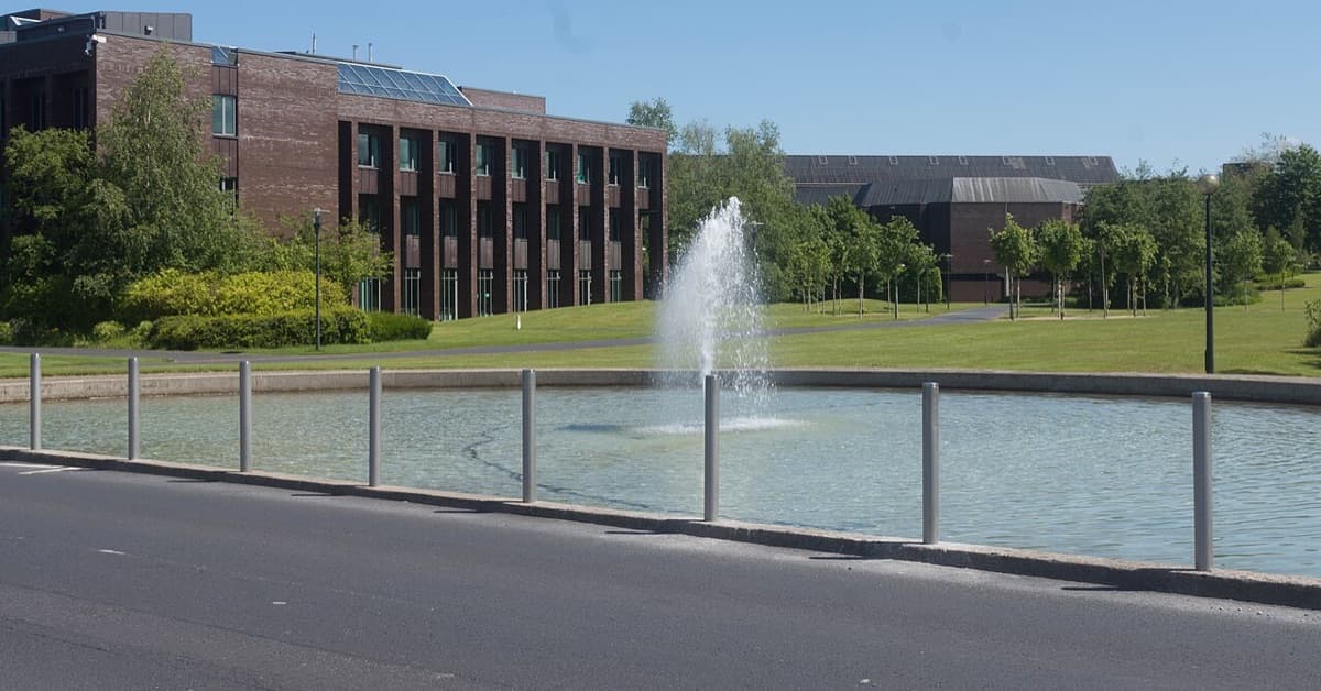 University of Limerick campus buildings with modern brick architecture beside a fountain and pond feature in daylight.