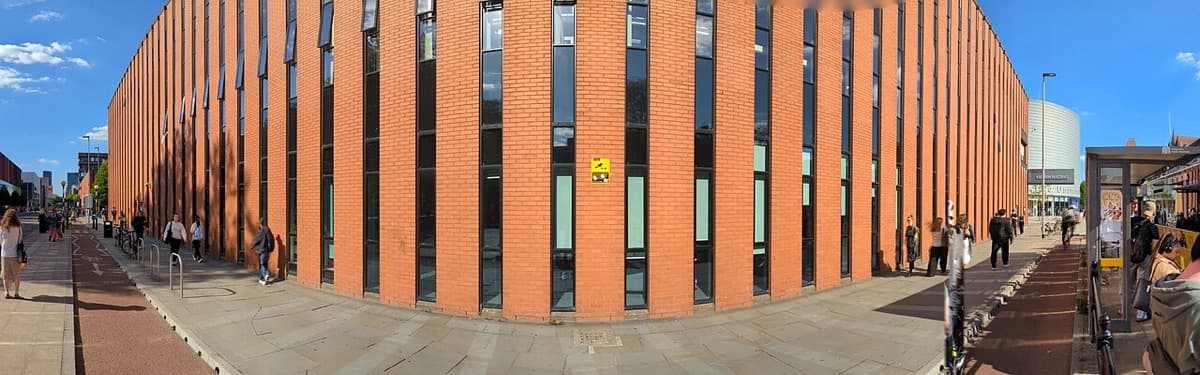 The Kilburn Building at University of Manchester, a modern orange-brick structure viewed from Oxford Road with clear horizontal lines.