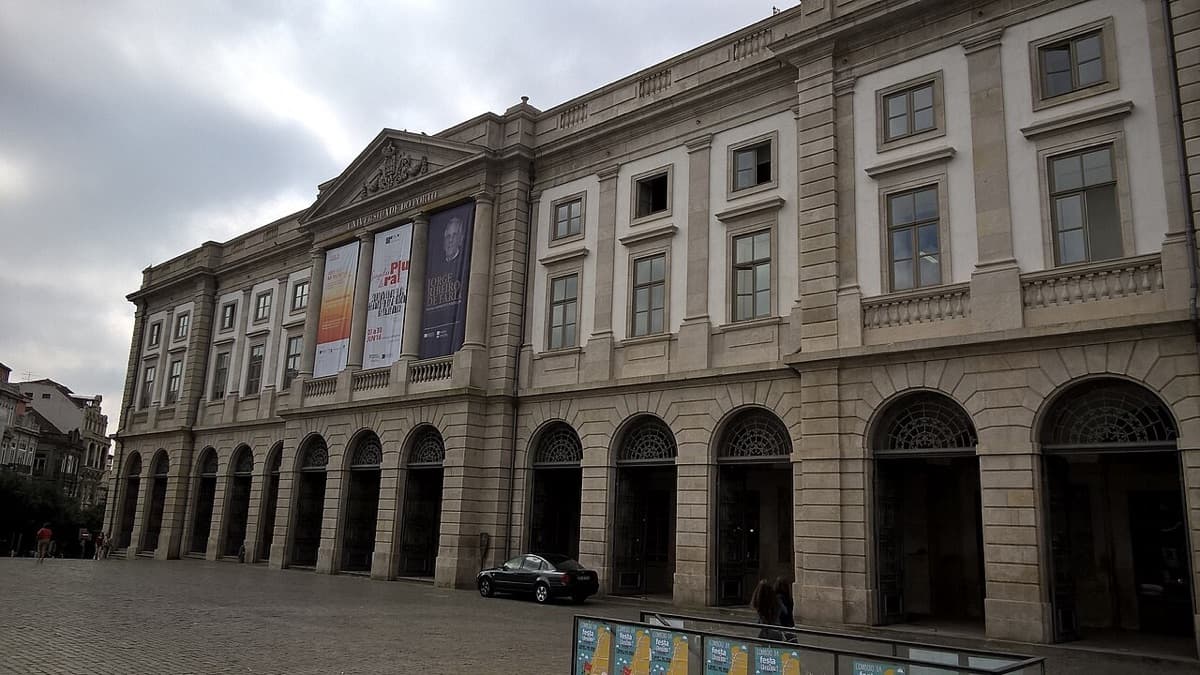 The neoclassical Reitoria building of the University of Porto, its arcaded stone facade running the length of the square.