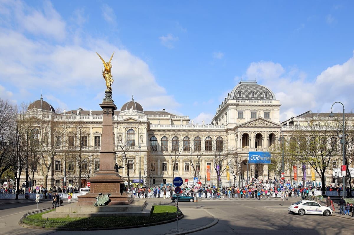 Iconic main building of University of Vienna showing grand neoclassical architecture with statue in the foreground and Austrian institutional character.